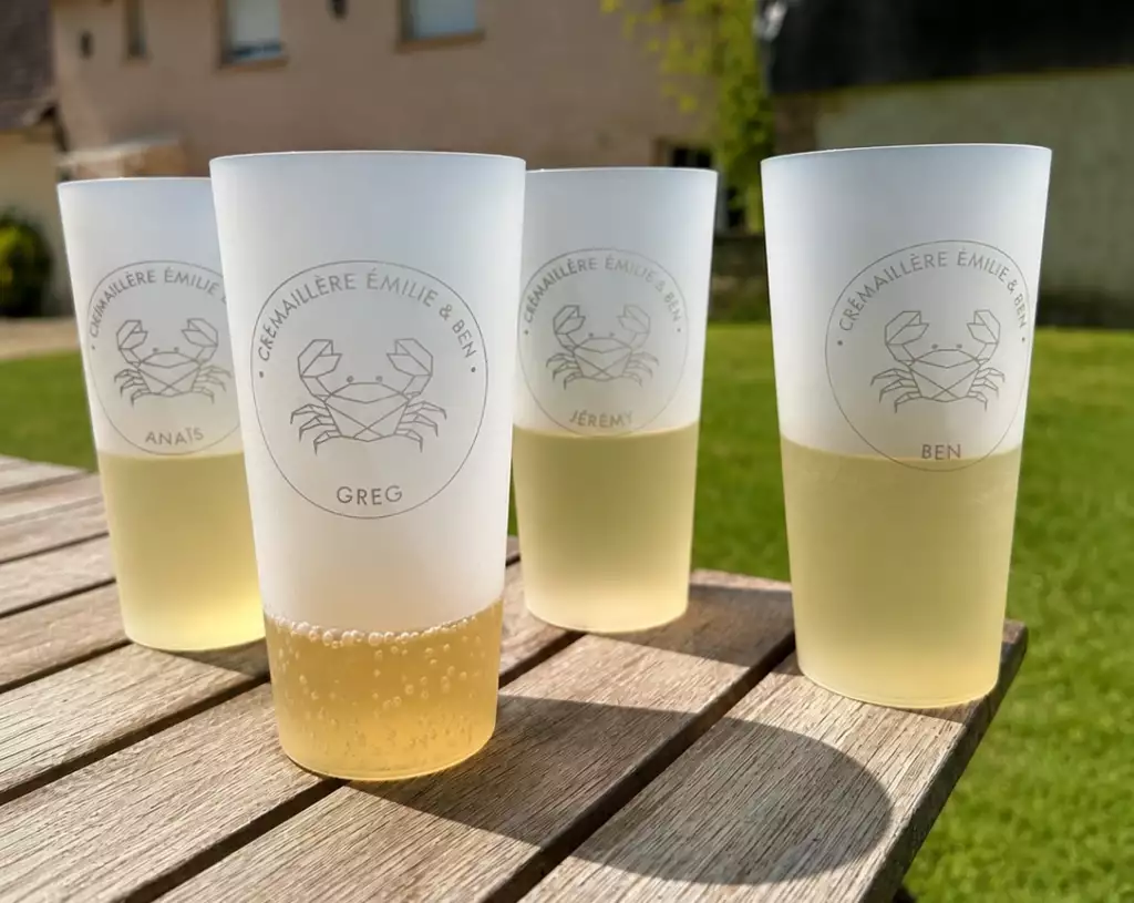 Gobelets personnalisés réutilisables avec gravure laser et prénom individuel, posés sur une table en bois en extérieur lors d’un événement convivial et élégant.