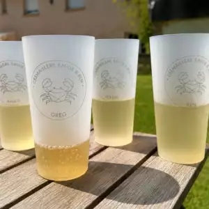 Gobelets personnalis&eacute;s r&eacute;utilisables avec gravure laser et pr&eacute;nom individuel, pos&eacute;s sur une table en bois en ext&eacute;rieur lors d&rsquo;un &eacute;v&eacute;nement convivial et &eacute;l&eacute;gant.